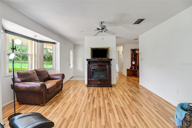 living room with a textured ceiling, light wood-type flooring, and ceiling fan