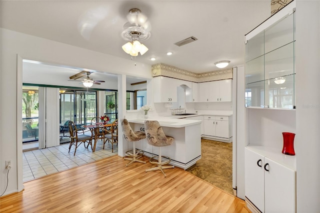 kitchen with kitchen peninsula, a breakfast bar, ceiling fan, light hardwood / wood-style flooring, and white cabinets