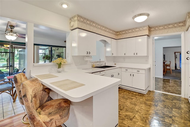 kitchen with kitchen peninsula, white cabinetry, sink, and ceiling fan