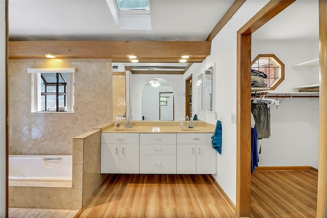 bathroom with a skylight, vanity, a relaxing tiled tub, and hardwood / wood-style flooring