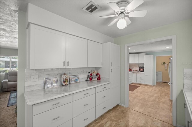 kitchen with white cabinets, ceiling fan, light stone countertops, and backsplash