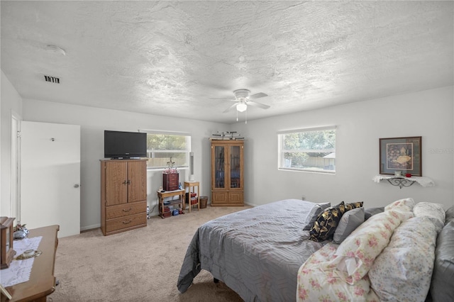 bedroom with a textured ceiling, light colored carpet, multiple windows, and ceiling fan