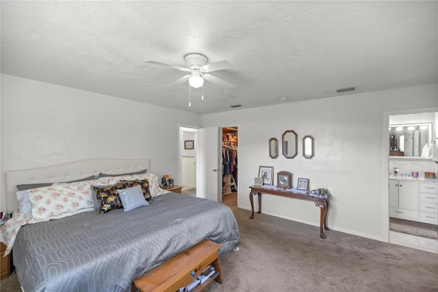 bedroom with ceiling fan, light colored carpet, a walk in closet, and ensuite bathroom