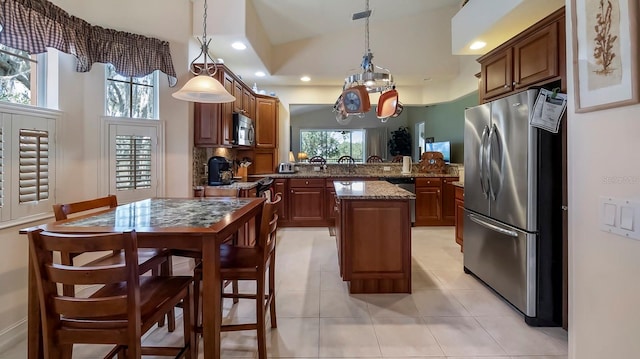 kitchen with light stone countertops, appliances with stainless steel finishes, decorative light fixtures, and a kitchen island