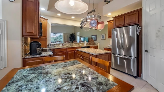 kitchen with pendant lighting, dark stone counters, light tile patterned floors, a kitchen island, and stainless steel refrigerator