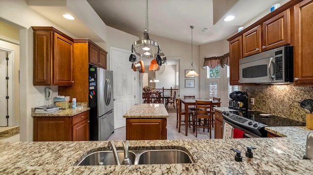 kitchen featuring light stone countertops, a center island, hanging light fixtures, stainless steel appliances, and backsplash