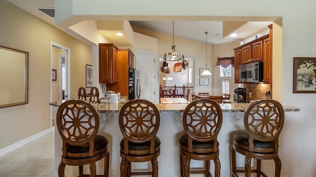 kitchen with kitchen peninsula, light stone counters, hanging light fixtures, and appliances with stainless steel finishes