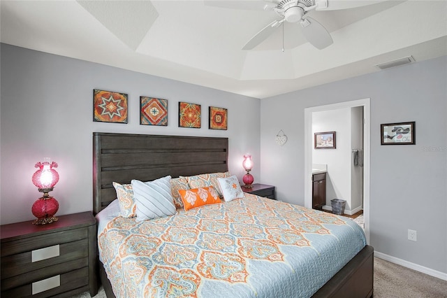 bedroom featuring a tray ceiling, connected bathroom, ceiling fan, and light colored carpet