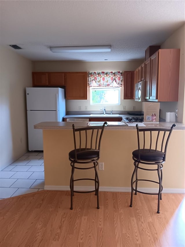 kitchen with sink, white fridge, light wood-type flooring, kitchen peninsula, and a breakfast bar area