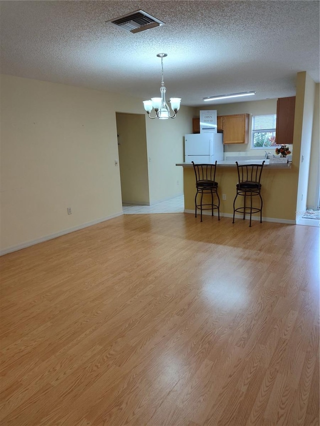 interior space with a notable chandelier, white refrigerator, light hardwood / wood-style flooring, and kitchen peninsula