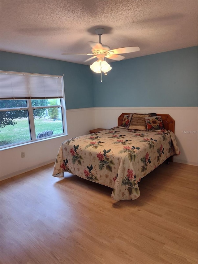 bedroom featuring ceiling fan, light hardwood / wood-style floors, and a textured ceiling