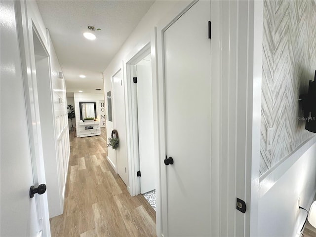 hall with a textured ceiling and light hardwood / wood-style flooring