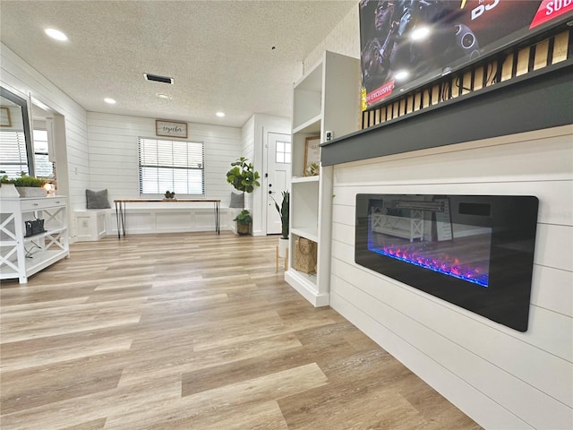 living room with a textured ceiling, light wood-type flooring, a glass covered fireplace, and a healthy amount of sunlight