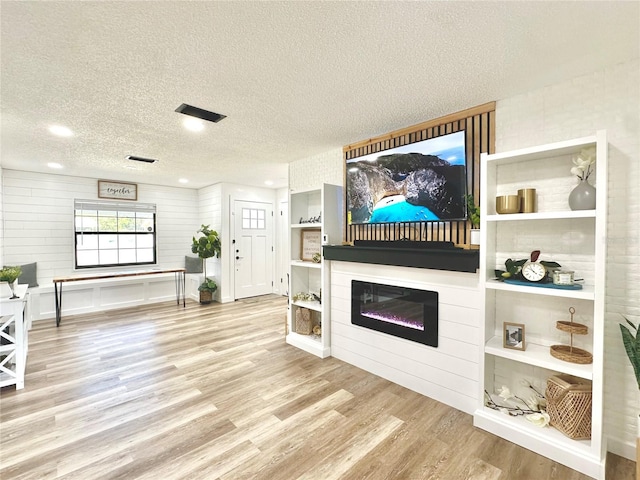 living area with light wood finished floors, visible vents, a textured ceiling, and a glass covered fireplace