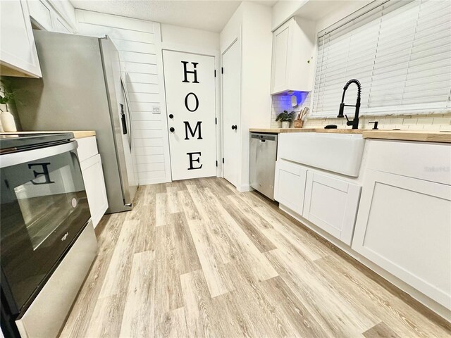 kitchen with stainless steel appliances, white cabinets, light wood-type flooring, and decorative backsplash