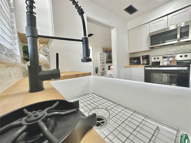 kitchen featuring appliances with stainless steel finishes, white cabinets, a textured ceiling, and decorative backsplash