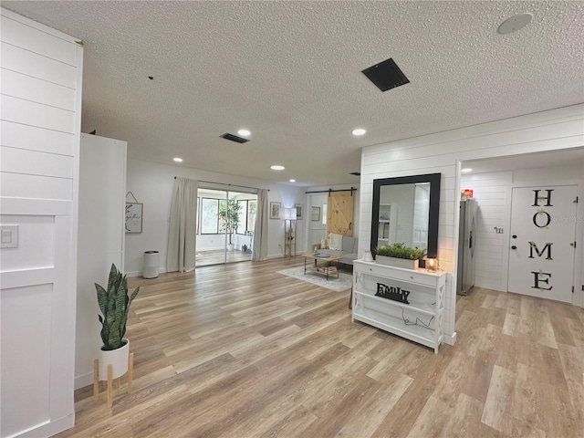 living room with light hardwood / wood-style floors, a barn door, and a textured ceiling