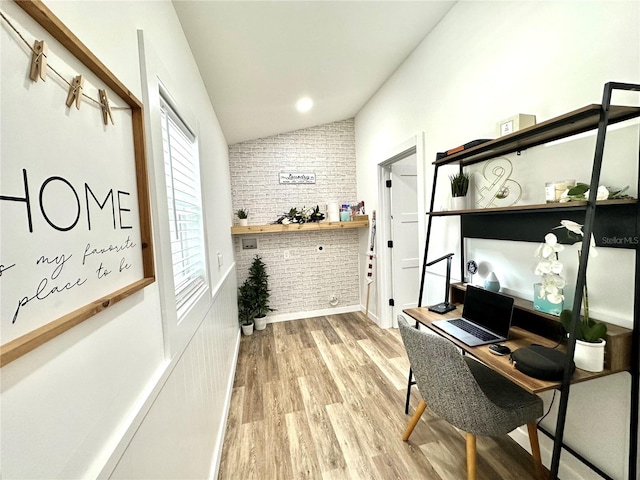 home office with hardwood / wood-style flooring, vaulted ceiling, and brick wall