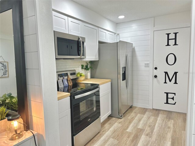 kitchen with white cabinetry, a textured ceiling, light wood-type flooring, appliances with stainless steel finishes, and backsplash