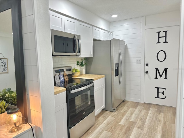 kitchen featuring light wood finished floors, backsplash, appliances with stainless steel finishes, white cabinetry, and a textured ceiling