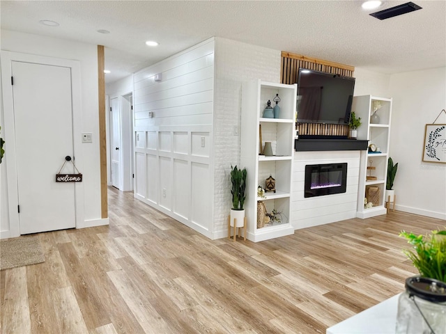 unfurnished living room featuring light wood-style floors, recessed lighting, a textured ceiling, and a glass covered fireplace