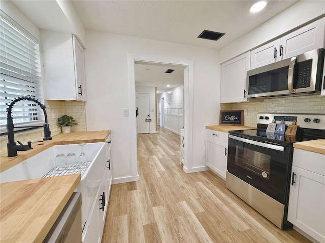 kitchen with stainless steel appliances, white cabinetry, and wooden counters