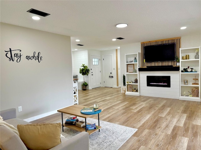 living room featuring visible vents, a fireplace, a textured ceiling, and wood finished floors