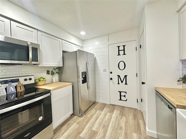 kitchen with light wood finished floors, butcher block countertops, appliances with stainless steel finishes, and white cabinets