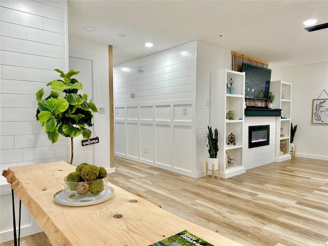 interior space with light wood-style floors, a glass covered fireplace, a textured ceiling, and recessed lighting