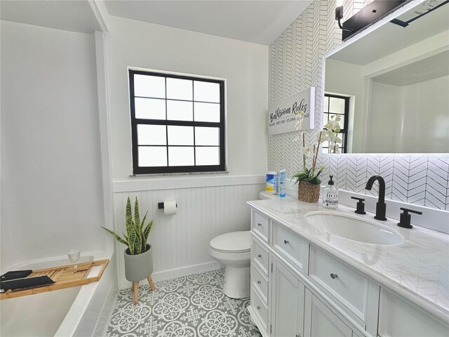 full bath with toilet, tile patterned flooring, vanity, and wainscoting