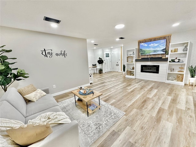 living room featuring light wood-type flooring, a glass covered fireplace, baseboards, and recessed lighting