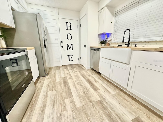 kitchen with appliances with stainless steel finishes, light wood-type flooring, decorative backsplash, and white cabinets