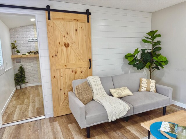 sitting room with vaulted ceiling, brick wall, a barn door, and wood finished floors