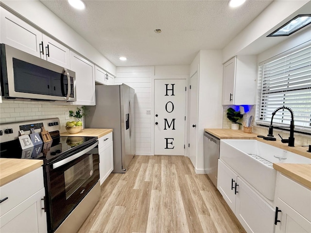 kitchen with appliances with stainless steel finishes, butcher block counters, white cabinetry, and a sink