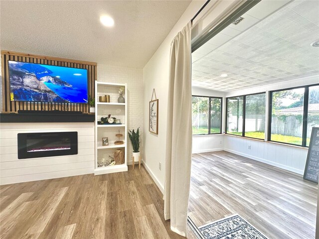 unfurnished living room featuring a textured ceiling, baseboards, wood finished floors, and a glass covered fireplace