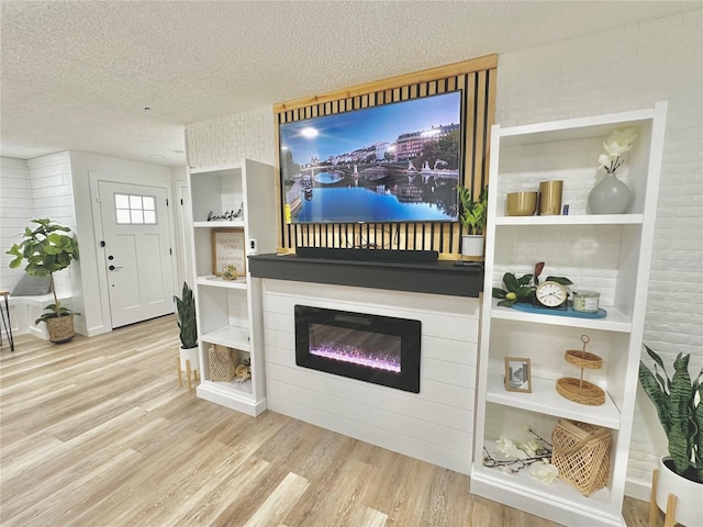 living area with a textured ceiling, light wood finished floors, and a glass covered fireplace