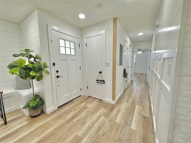 foyer entrance with a textured ceiling, baseboards, and light wood-style floors