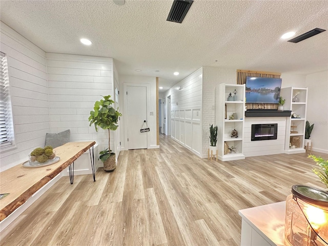 living area with visible vents, a glass covered fireplace, wood walls, a textured ceiling, and light wood-type flooring