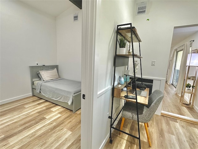 bedroom with light wood-style floors, a wainscoted wall, and visible vents