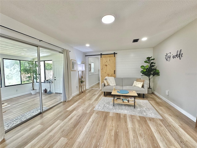 living area featuring visible vents, light wood-style flooring, a textured ceiling, and a barn door
