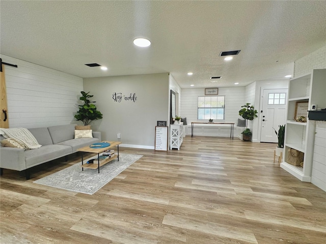 living room with a fireplace, recessed lighting, light wood-style flooring, a barn door, and a textured ceiling
