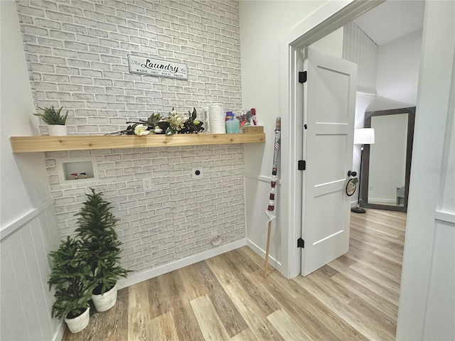 interior space featuring light wood finished floors, brick wall, and wainscoting