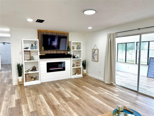 living room with light wood finished floors, baseboards, a textured ceiling, and a glass covered fireplace