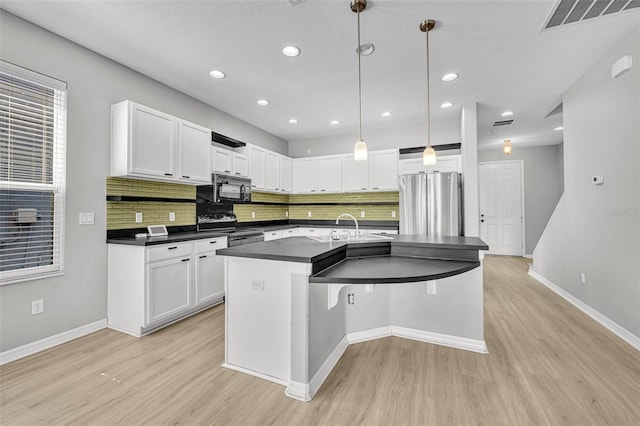 kitchen featuring light wood-type flooring, stainless steel appliances, decorative light fixtures, white cabinets, and an island with sink