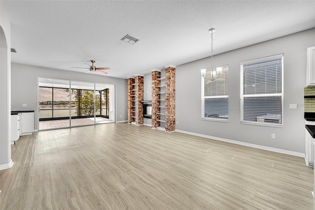 unfurnished living room featuring a textured ceiling, ceiling fan with notable chandelier, a fireplace, and light hardwood / wood-style flooring