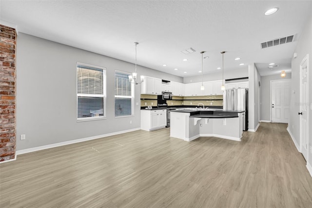 kitchen featuring appliances with stainless steel finishes, light wood-type flooring, a kitchen island with sink, white cabinets, and hanging light fixtures