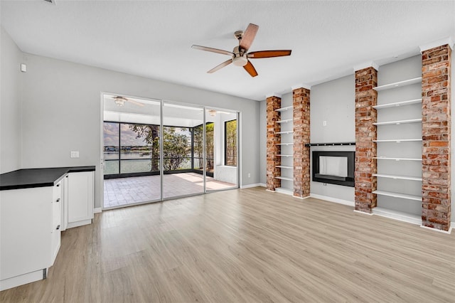 unfurnished living room featuring ceiling fan, a large fireplace, a textured ceiling, and light hardwood / wood-style flooring