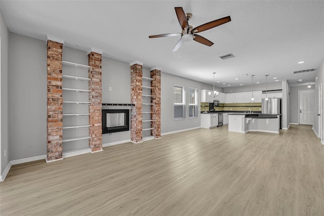 unfurnished living room with a large fireplace, light hardwood / wood-style flooring, a textured ceiling, and ceiling fan with notable chandelier