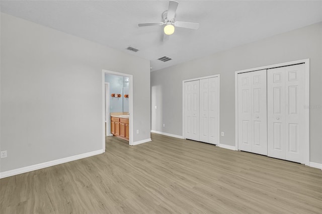 unfurnished bedroom with ensuite bath, ceiling fan, light hardwood / wood-style flooring, and multiple closets