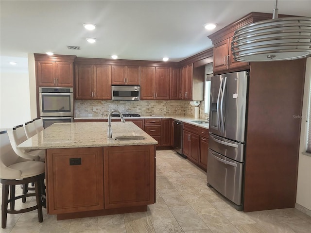 kitchen with a kitchen bar, sink, appliances with stainless steel finishes, an island with sink, and decorative backsplash